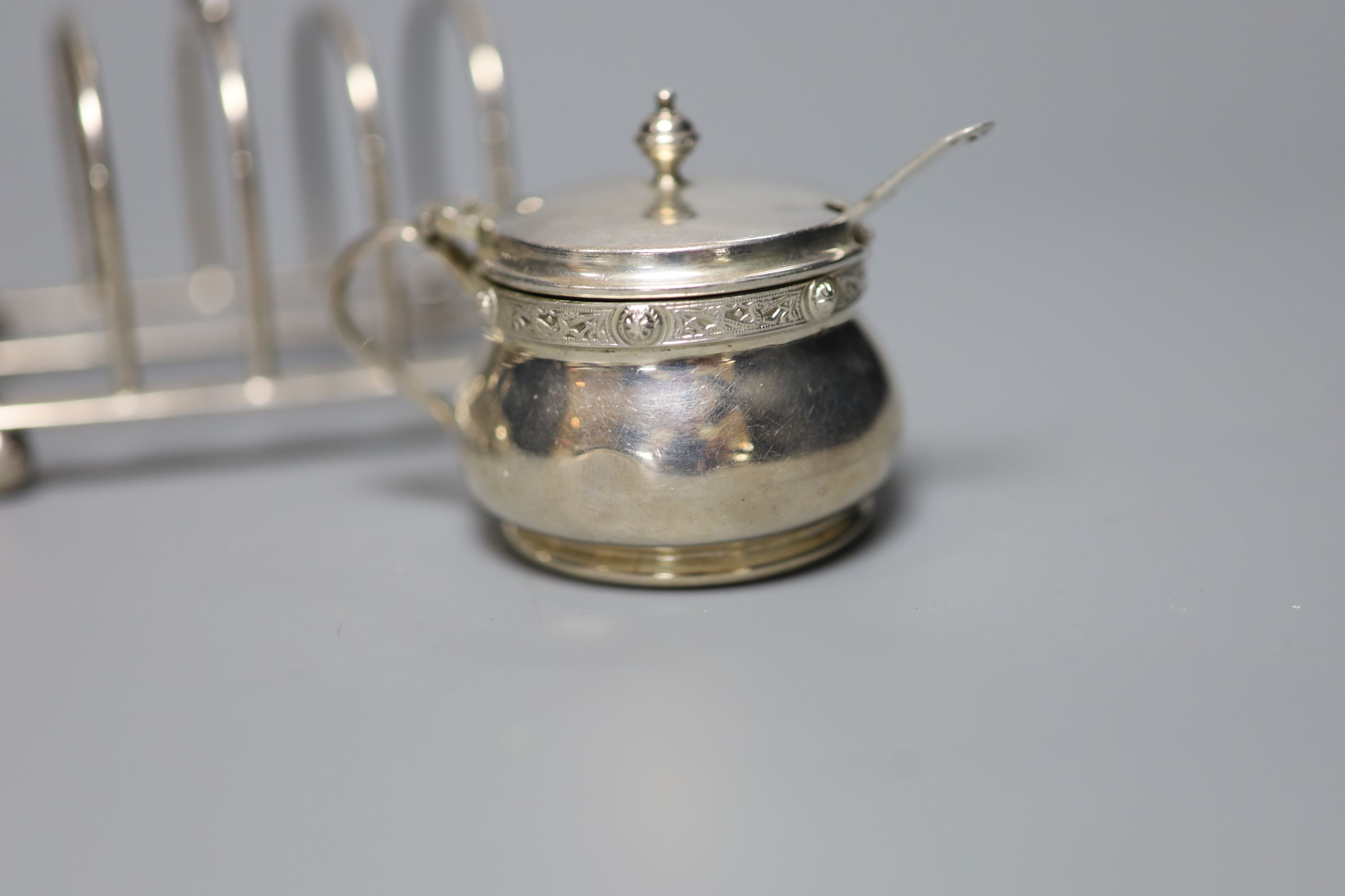 A pair of George V silver toast racks, a silver tea strainer and a silver three piece condiment set.